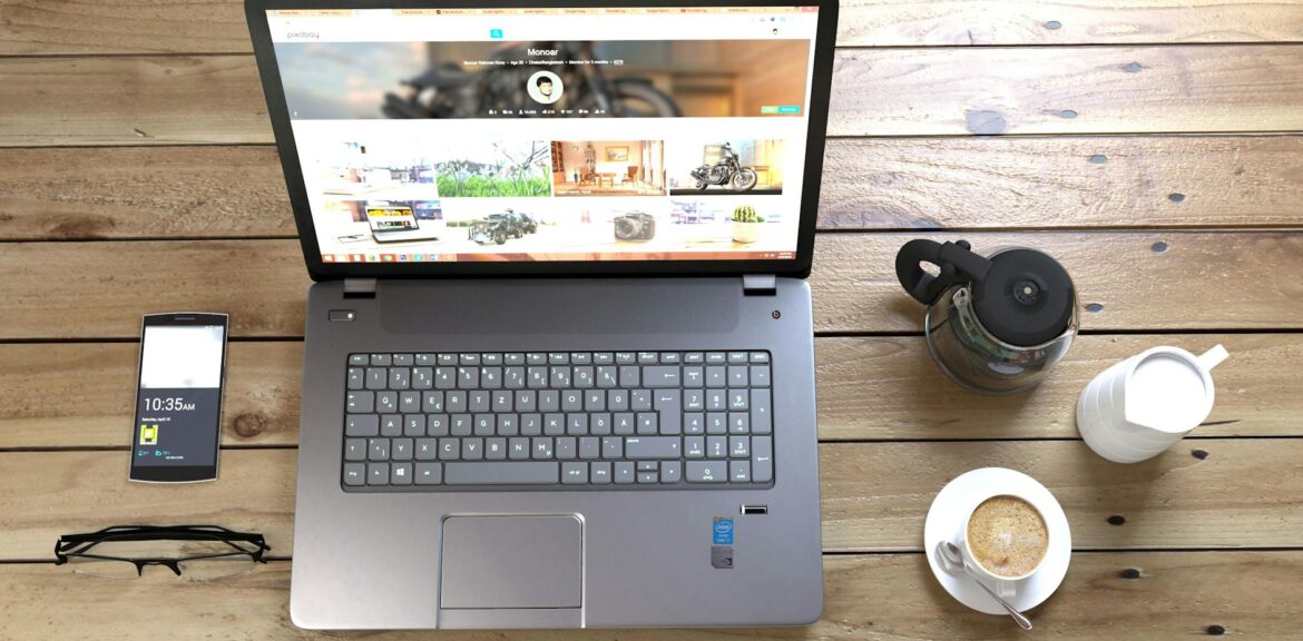 silver laptop next to coffe cup smartphone and glasses